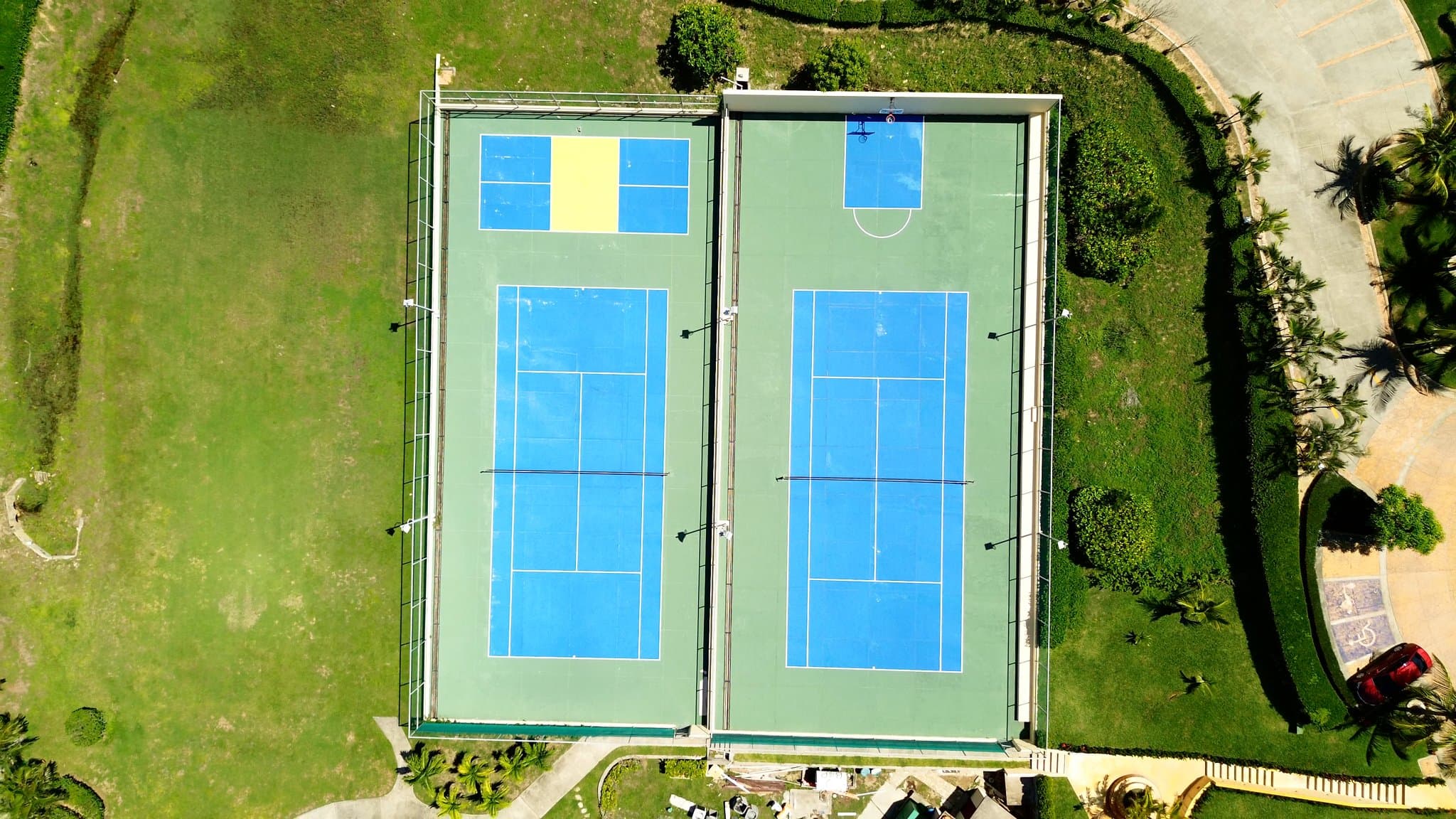 Outdoor tennis court surrounded by lush greenery under tropical skies.