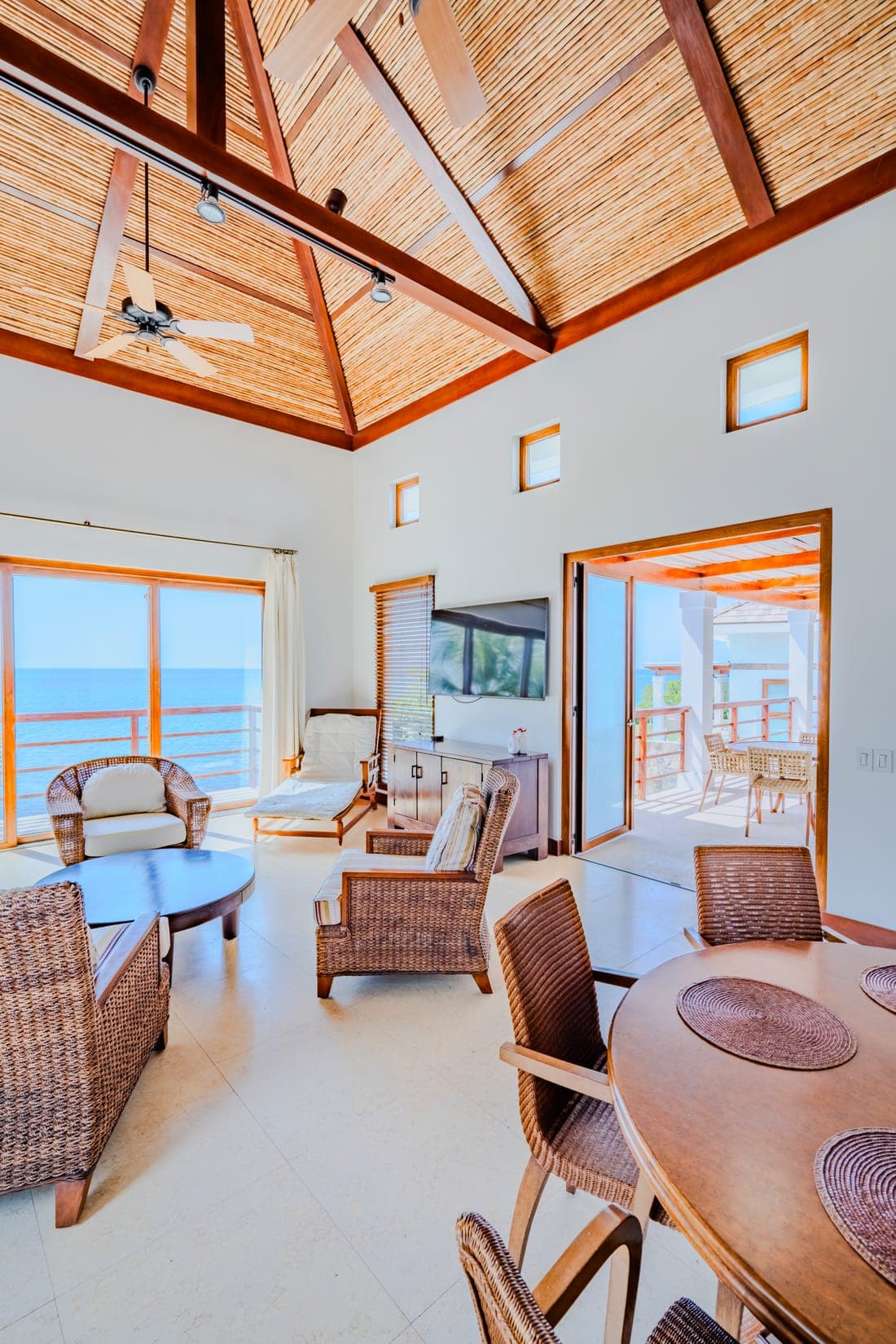A villa living room under a vaulted timber ceiling, opening onto an ocean-front terrace